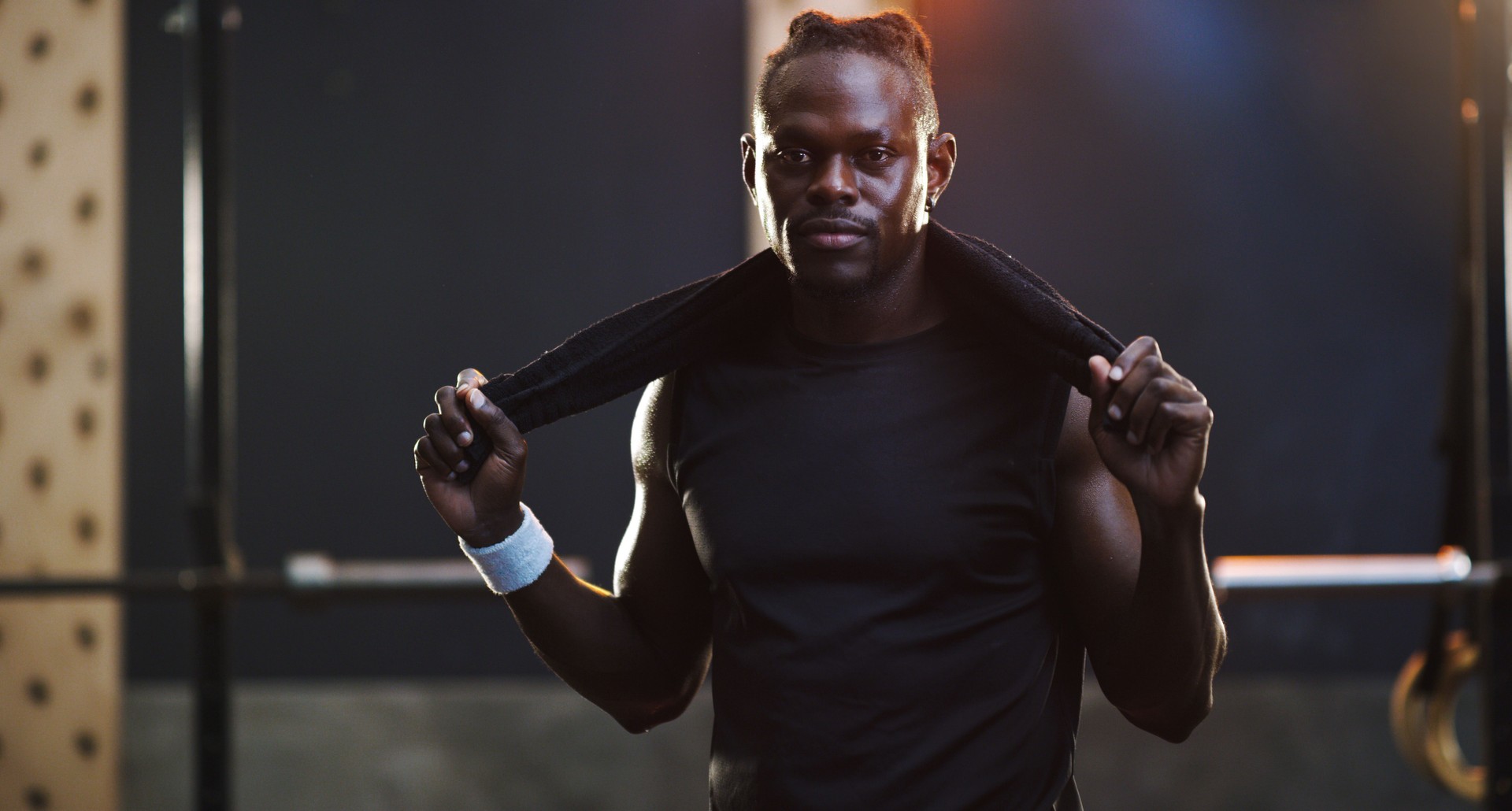 Portrait of a muscular young man standing with a towel around his neck in a gym